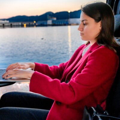 Woman using a laptop while sitting in the back seat of a Toyota Proace Verso transfer van.