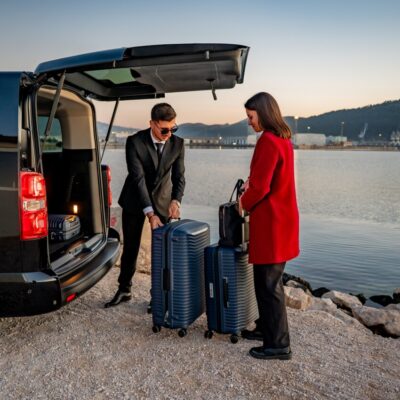 Driver loading suitcases into the back of a Toyota Proace Verso transfer van near the coast.