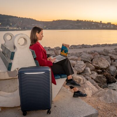 Business woman with suitcase using a tablet while waiting by the waterfront at sunset – private transfer service concept